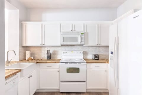 The clean white appliances are broken up with a tumbled marble backsplash and sealed customized butcher block countertops and an apron sink.