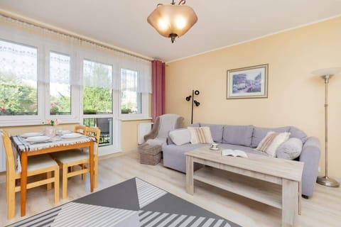 A bright living room with a dining table, gray sofa, and a large window, creating a cozy and inviting space.
