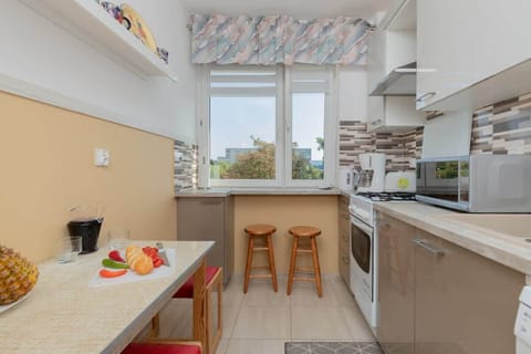 A kitchen layout with a breakfast bar, wooden stools, and a window overlooking a garden.
