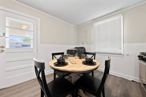 The dining area is furnished with a round wooden table and four black chairs, set with plates, glasses, and napkins for four.