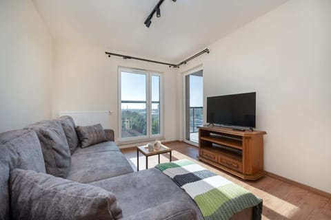 A cozy living room with a grey sectional sofa, a wooden TV stand, and a large window bringing in natural light.
