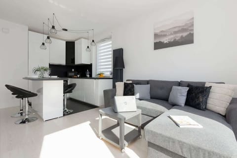 A modern living room with a grey sofa, a glass coffee table, and bright natural light streaming in through large windows.
