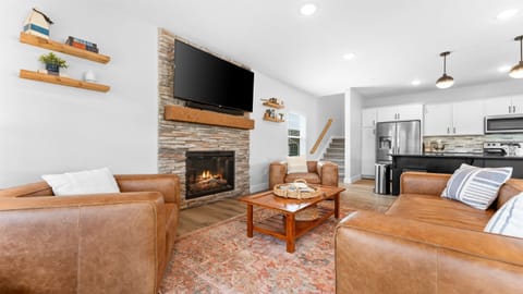 Cozy living room with fireplace & big-screen Roku TV, open to the kitchen.