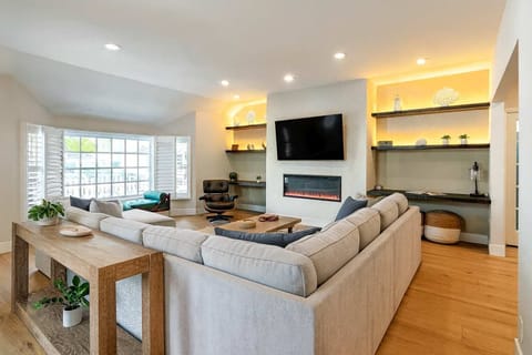 Elegant, modern living space featuring custom shelving, a large sectional, and a glowing fireplace ambiance.