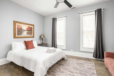 The bedroom's charm with a great window allowing natural light, complemented by a bedside table and lamp, a dresser for storage, and the added comfort of a futon.