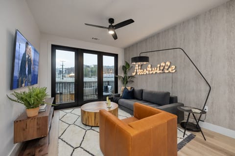 Open concept living area with smart TV, comfortable seating, designer decor, natural lighting, and access to private patio.