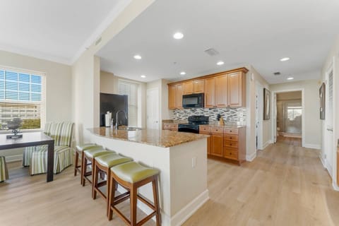 This open floor plan features a breakfast bar leading to a modern kitchen, well-lit with recessed ceiling lighting.