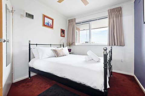 The cosy bedroom features a queen bed, ceiling fan and views across North Fitzroy.