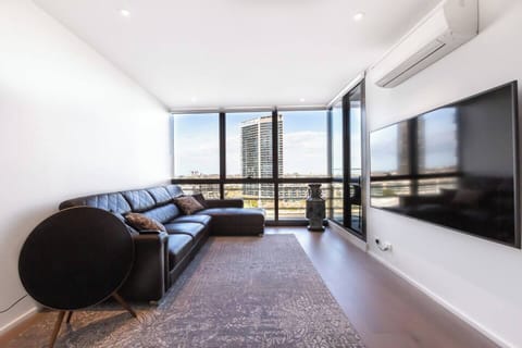 The living room is bright and spacious, offering an L-shaped lounge, large wall-hung TV and split-system heating and cooling.