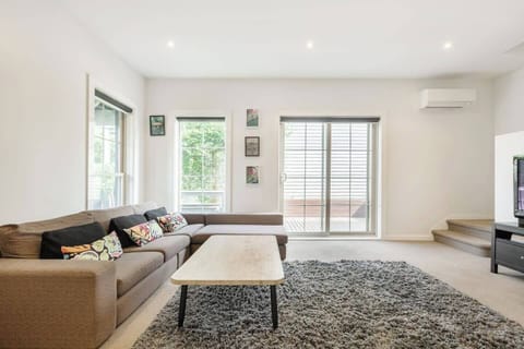 A downstairs living area provides an open plan space filled with natural light, and an L-shaped couch that faces a flat-screen TV with Foxtel