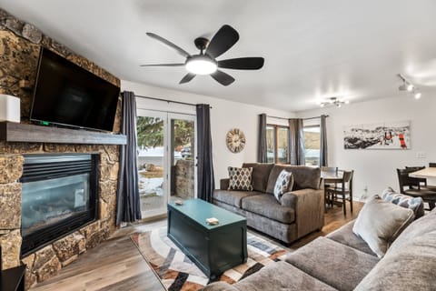 Cozy and modern living room with a rustic stone fireplace, wall-mounted TV, plush seating, and large windows offering a scenic, snowy view — perfect f