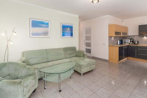 A spacious living room with a green sectional sofa, a coffee table, and an open-plan connection to the kitchen.
