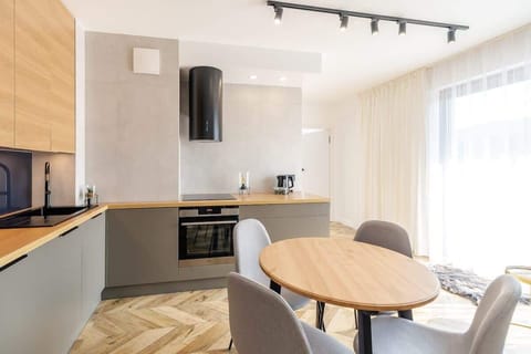 A closer view of the open kitchen with wooden cabinets, built-in appliances, and a small dining table. Large windows illuminate the space.
