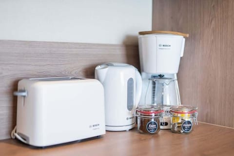 A coffee and tea station featuring a toaster, kettle, and jars of coffee and tea, neatly arranged on a wooden countertop.
