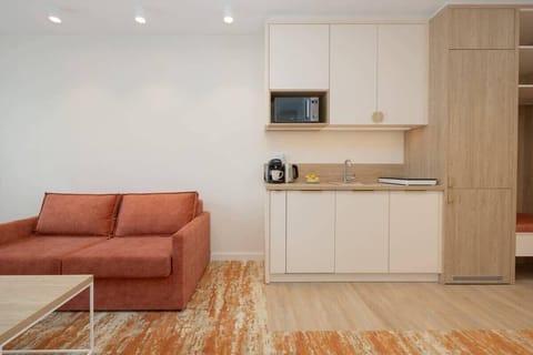 A compact open-plan living and kitchen area with an orange sofa, a coffee table, and a modern kitchenette.
