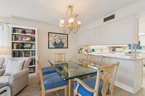 - Dining area with glass top table blue cushioned chairs and chandelier light  
- Open layout connects to living room and kitchen for seamless guest experience  
- A welcoming spot for shared meals and gatherings during a coastal vacation  