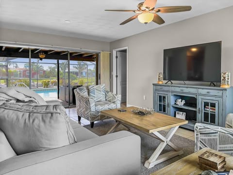 living room with large TV and sliding doors leading out to pool.
