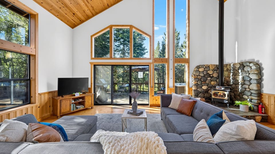 Soaring great room with floor-to-ceiling windows, warm wood accents, and direct access to the deck.