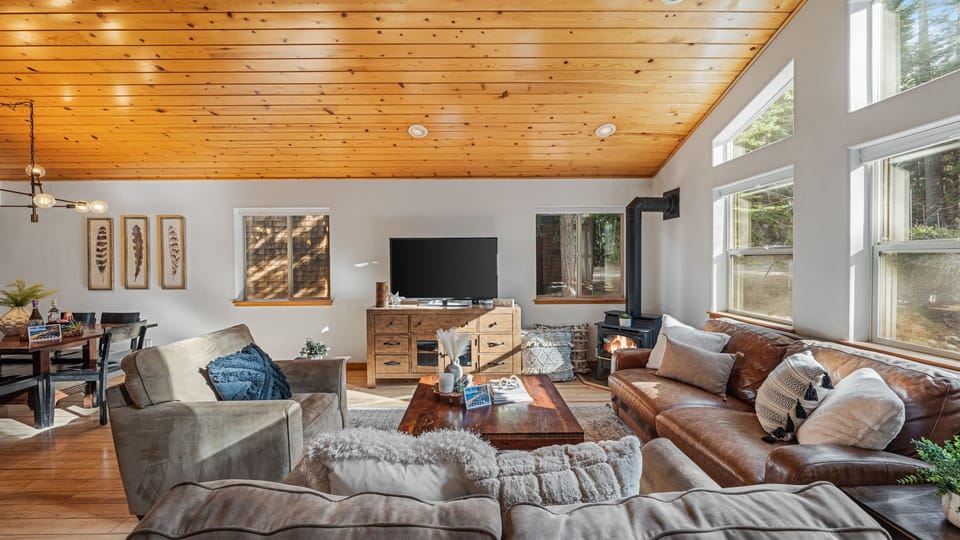 Sun-filled living area with vaulted wood ceilings and a cozy fireplace.