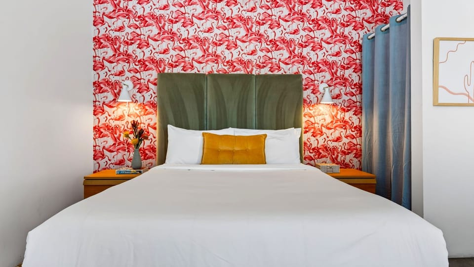 A queen bed anchors the studio, with bold flamingo wallpaper adding a playful pop of personality.