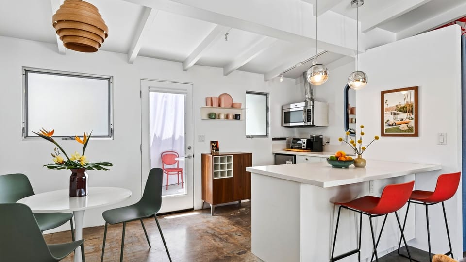 A bright open layout connects the kitchen and dining area, with bold red barstools and playful mid-century style throughout.