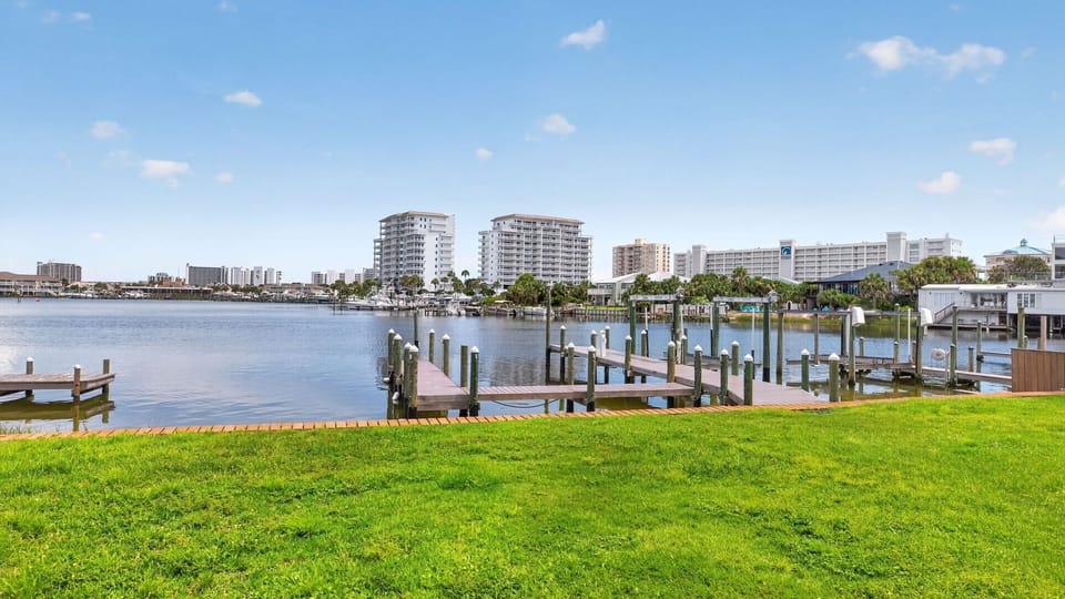 A lush waterfront lawn overlooks the calm waterway and surrounding docks, with coastal views stretching across the harbor.