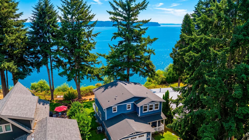 Aerial views showcase the waterfront home surrounded by towering evergreens and the sparkling Sound beyond.