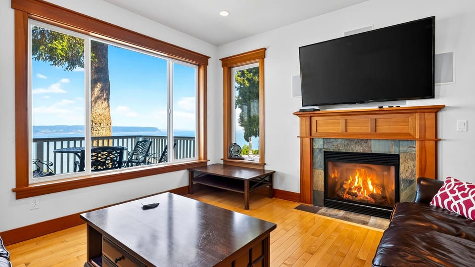 Cozy up by the fireplace while expansive windows frame tranquil views across the Sound.