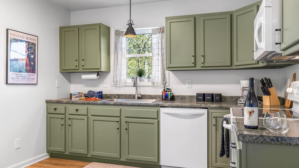 Fully equipped kitchen with stove, dishwasher, and bold matcha cabinets.