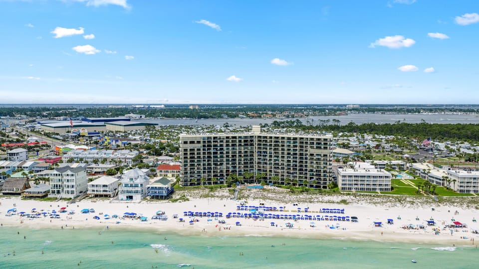 Aerial view of the beachfront area with turquoise Gulf waters, nearby resorts, and coastal attractions close by.