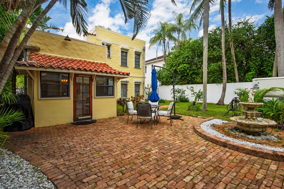 On either side of the fountain sit two cozy chairs, each equipped with a chic umbrella for shade, creating an ideal area for unwinding.