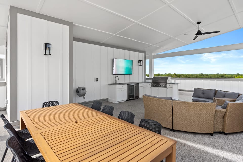 Covered rooftop patio with outdoor kitchen, TV, and lounge seating—perfect for dining, grilling, and relaxing with a view.