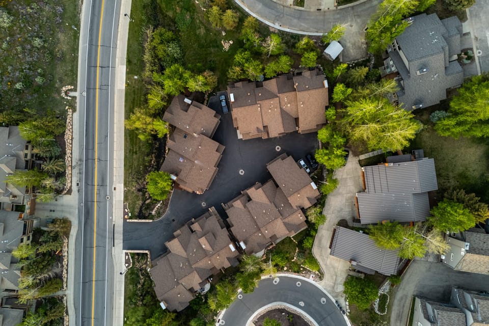Overhead drone shot of the neighborhood and surrounding forested landscape.