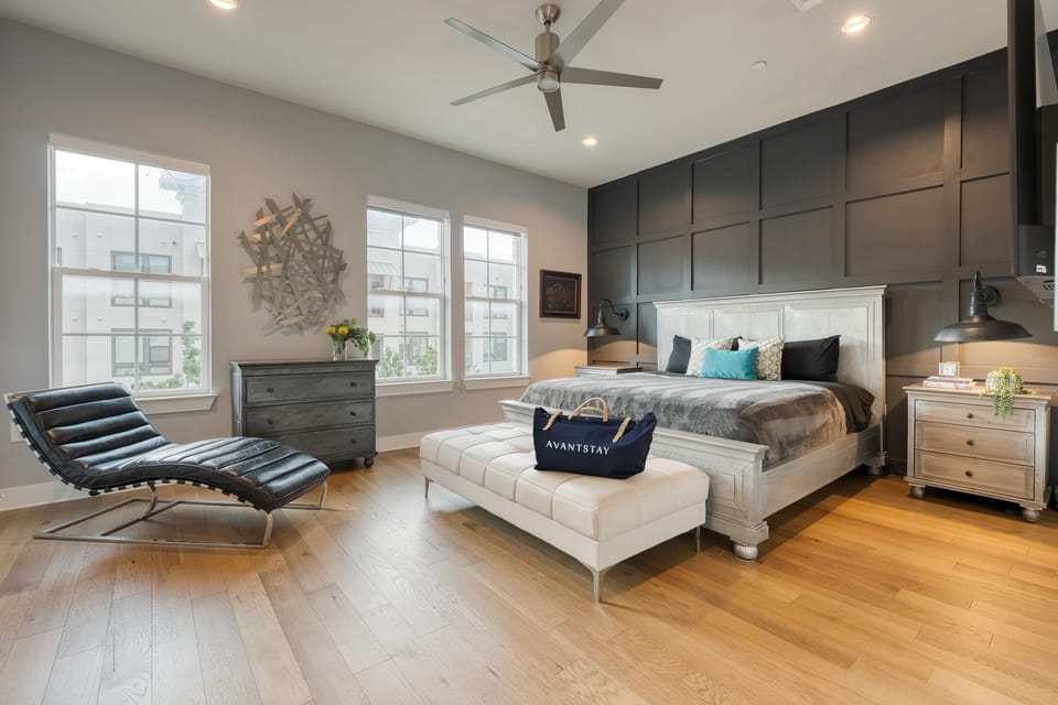 Primary bedroom features a king bed, TV, leather chaise lounge, upholstered bench and an ensuite bathroom.