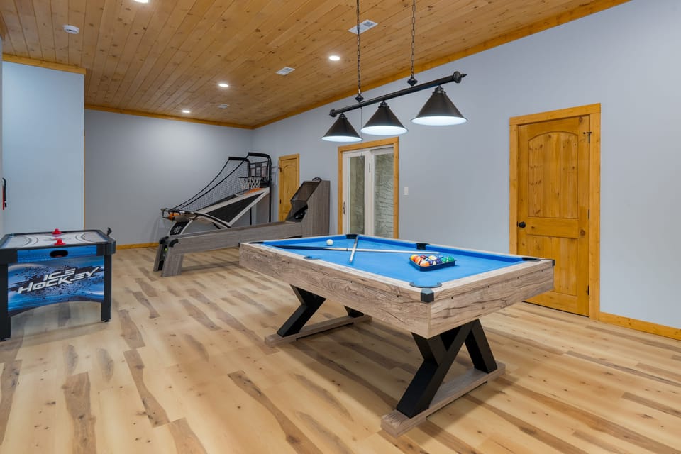 A spacious game room featuring a pool table, basketball arcade game, and air hockey table.