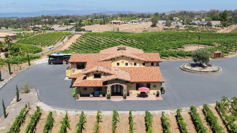 An aerial view showcases the Mediterranean-style home surrounded by rolling vineyard rows and expansive countryside. (Villa)