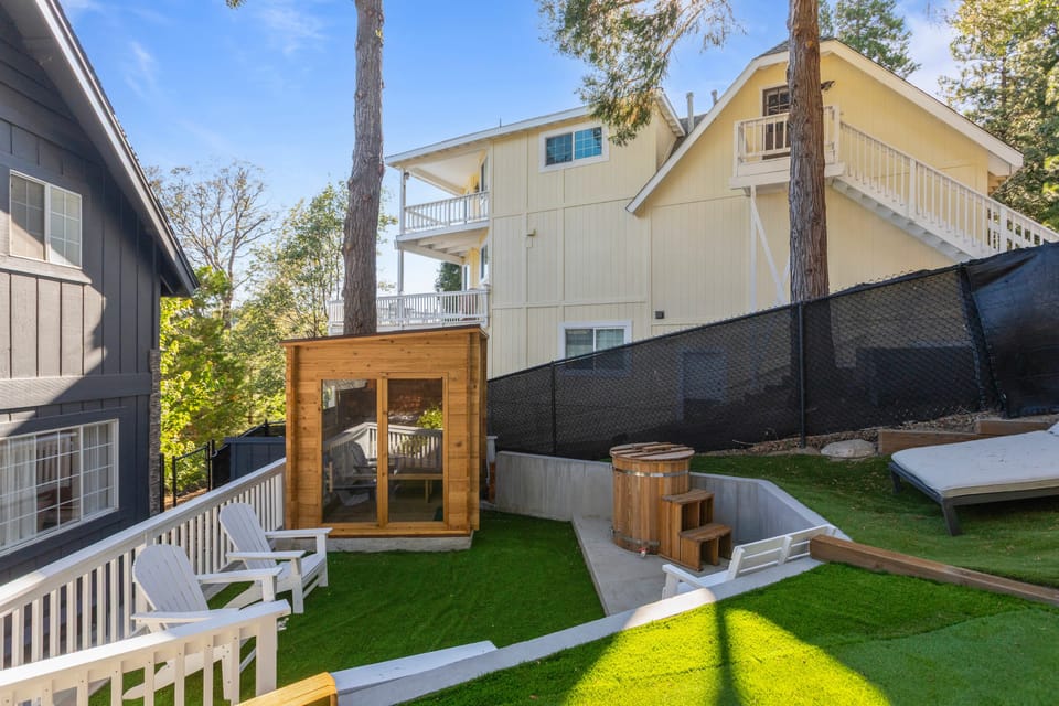 Fenced backyard with turf lawn, hanging lights, and sauna.