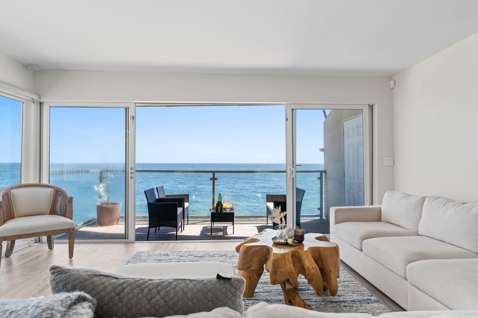 Cozy living room featuring a plush couch, fireplace, TV, ocean views, and access to the balcony.