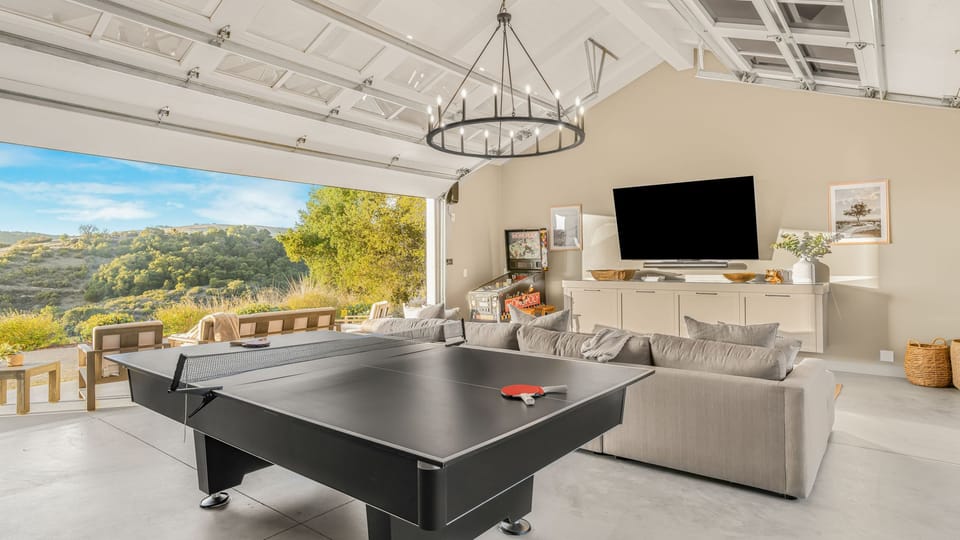 The game room features a sectional couch, a ping pong table, a TV, and an arcade game. (View House)