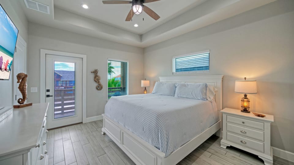 Bedroom with a king bed, ceiling fan, TV, balcony access, and an ensuite bathroom.