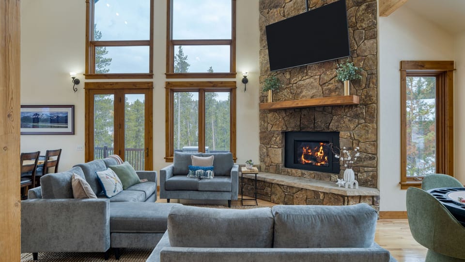 Living area with large windows, a fireplace, and a TV.
