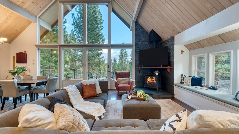 Cozy living room with soaring windows, forest views, and a wood-burning stove for perfect Tahoe nights.