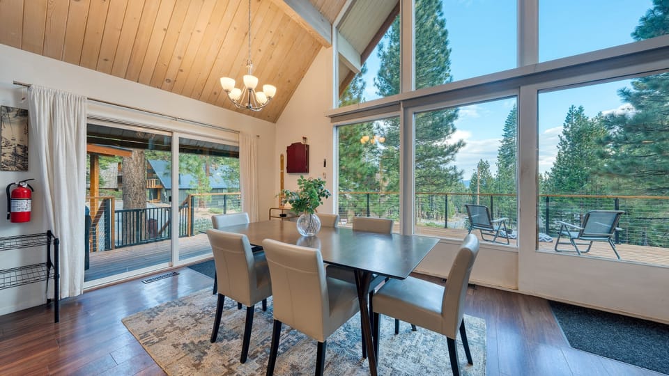 Bright dining area framed by panoramic windows and vaulted ceilings, offering immersive woodland views.