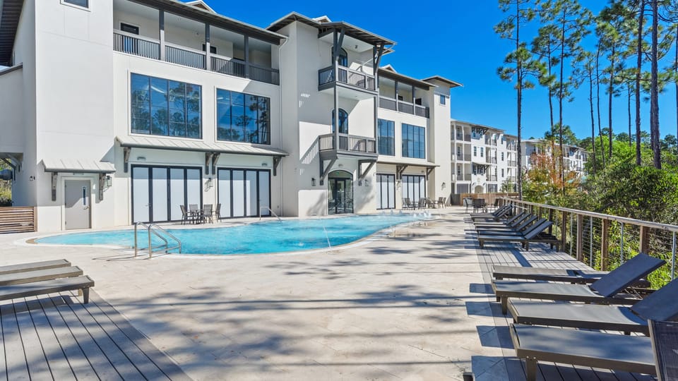 Resort-style community pool with ample lounge seating and a peaceful wooded backdrop.