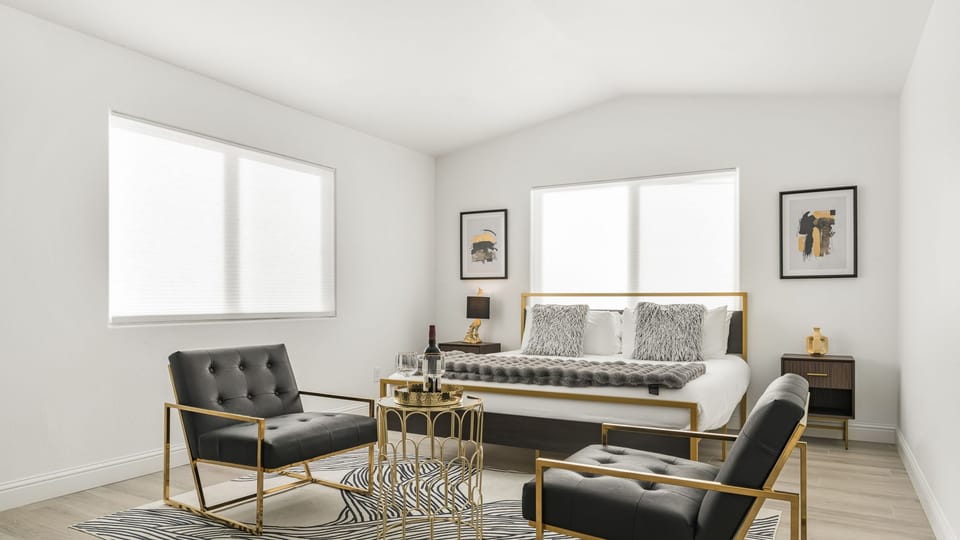 The primary bedroom features a king bed, gold accent chairs, and a small table set.