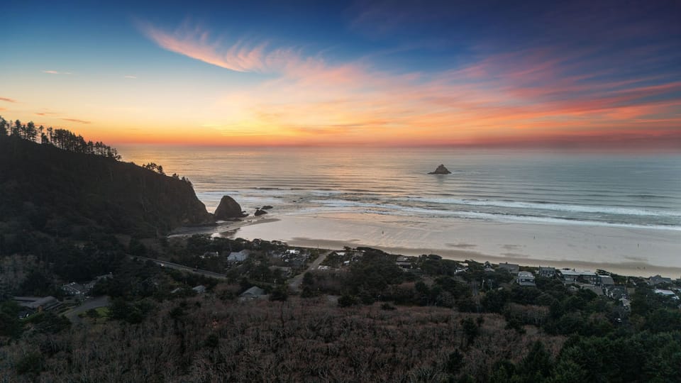 Scenic view of a dramatic sunset over the ocean and forested cliffs.