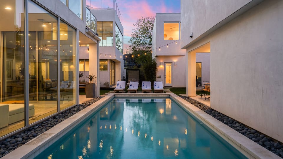 Shared outdoor retreat with a sleek pool, lounge chairs, and glowing string lights.