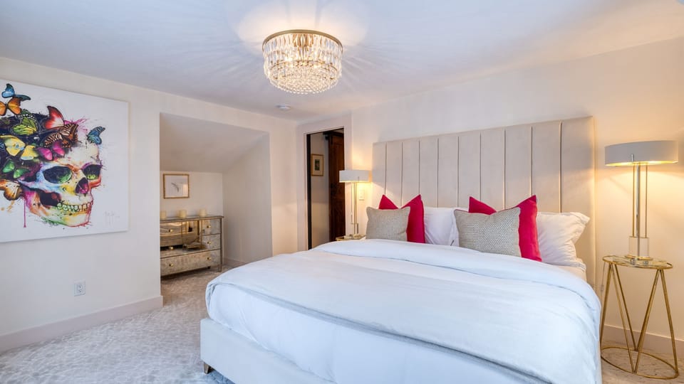 The bedroom features a king bed, white decor, and pink accent pillows.