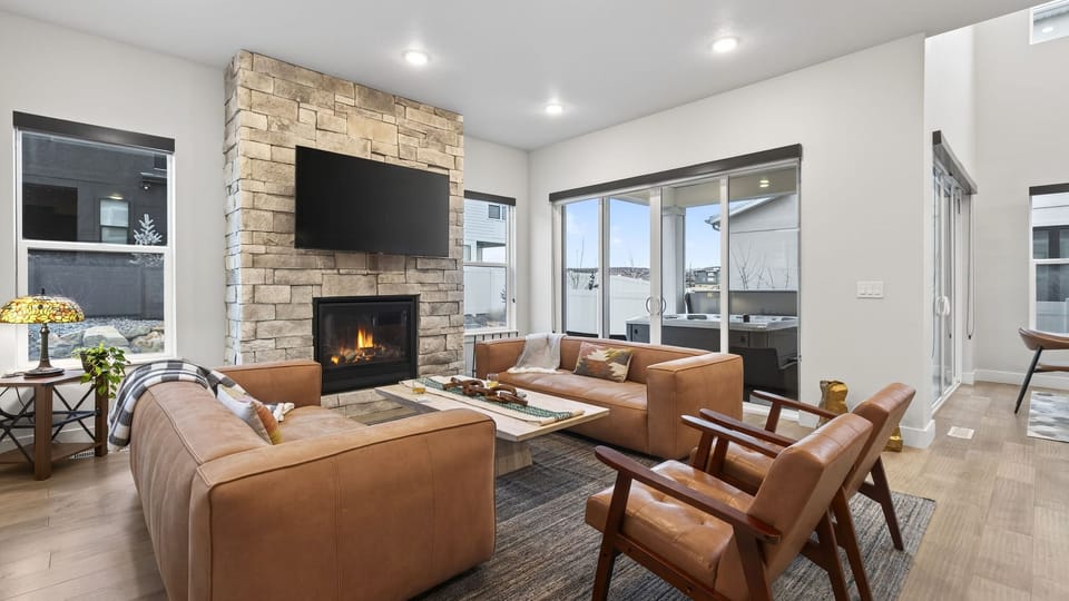Warm, modern living room with a stone fireplace, plush seating, and seamless access to the patio and hot tub—perfect for cozy nights after a day in Park City.