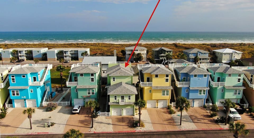 Main House: Aerial shot highlighting the colorful beach house within a coastal neighborhood.